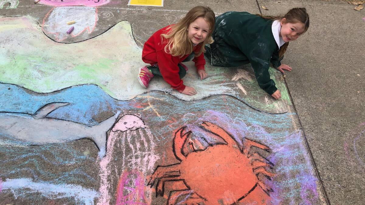 Eliza and Mila get chalky while finishing off their pavement chalk drawing. Picture supplied.